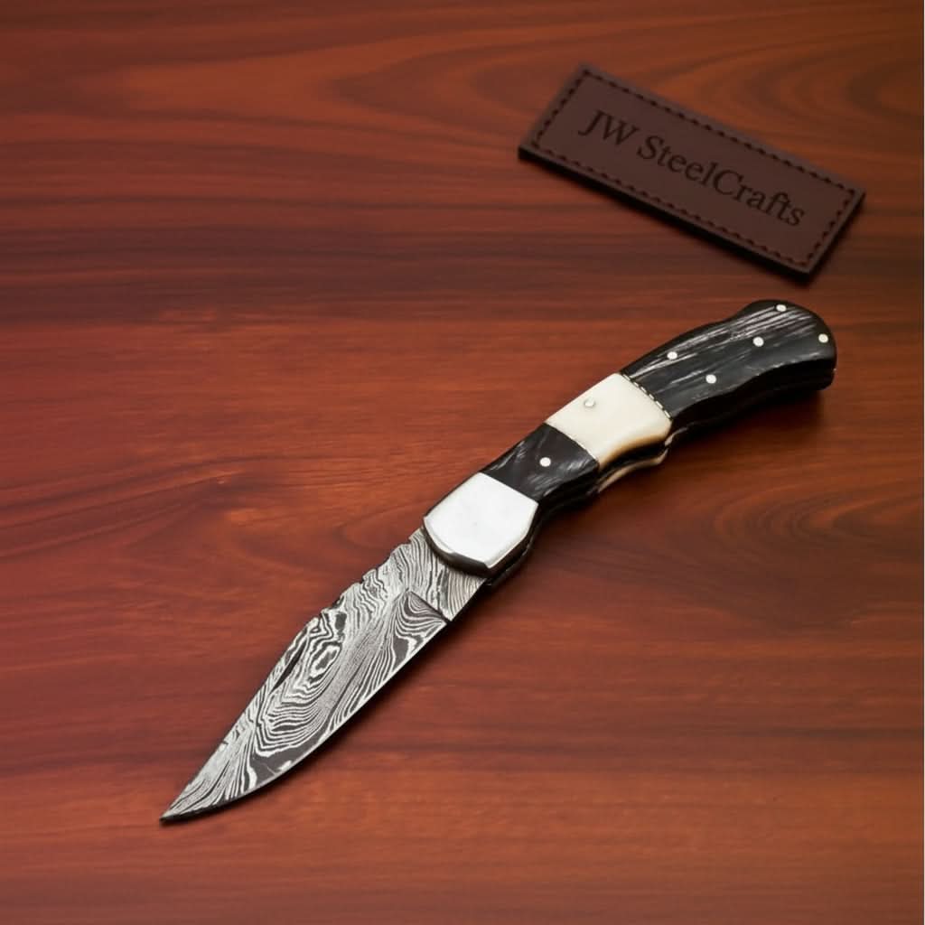     Oaktrail custom Damascus knife with ebony scales and pointed steel blade photographed indoors