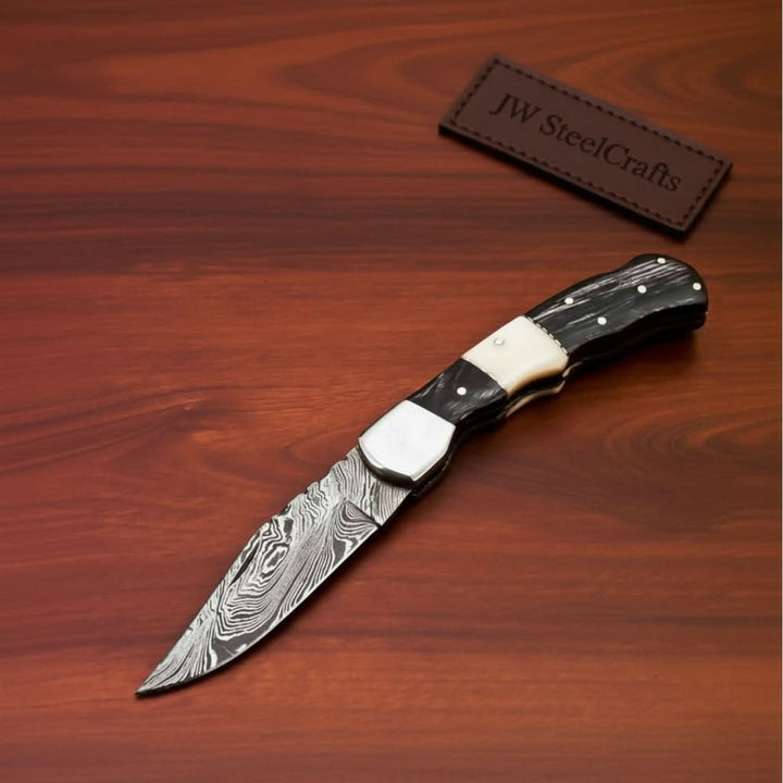     Oaktrail custom Damascus knife with ebony scales and pointed steel blade photographed indoors