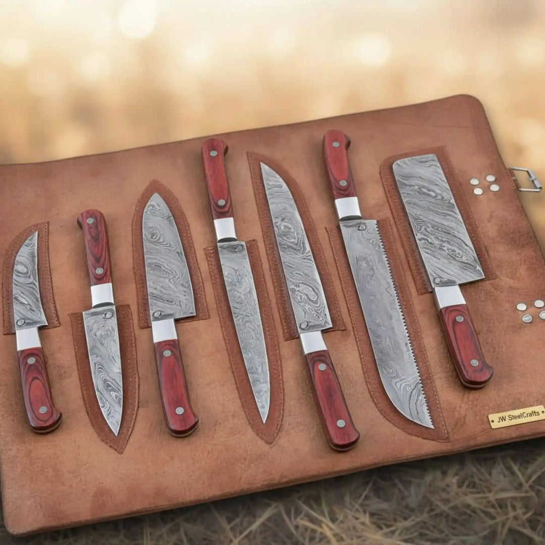 Top-down view of complete Damascus steel kitchen knife set with bold red pakkawood handles and silver bolsters displayed in a premium tan full-grain leather roll with bokeh background
