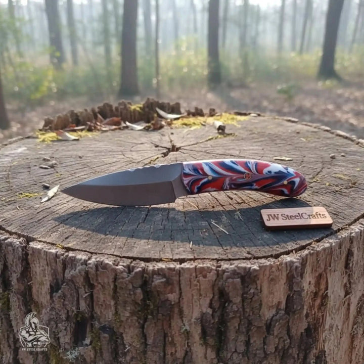 resin handle knife display showing a dark blade and colorful red blue grip on a forest tree stump.