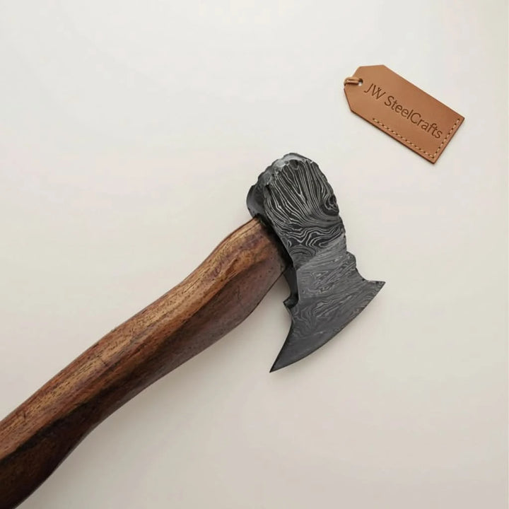 Thornforge-inspired Nordic Damascus hand axe with etched steel wave patterns and rustic forest presentation.