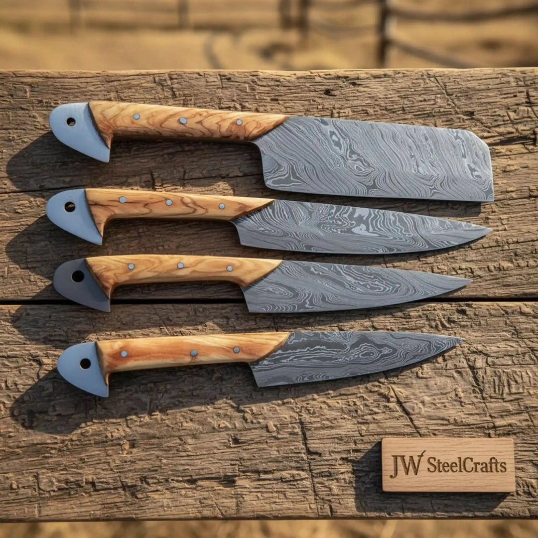 Four Damascus kitchen knives with olive wood handles displayed horizontally on weathered wooden table.