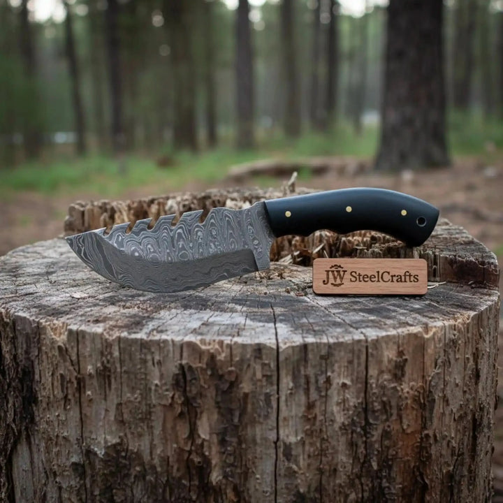 Black grip custom survival cleaver featuring a patterned steel blade and aggressive spine notches in a forest setting.