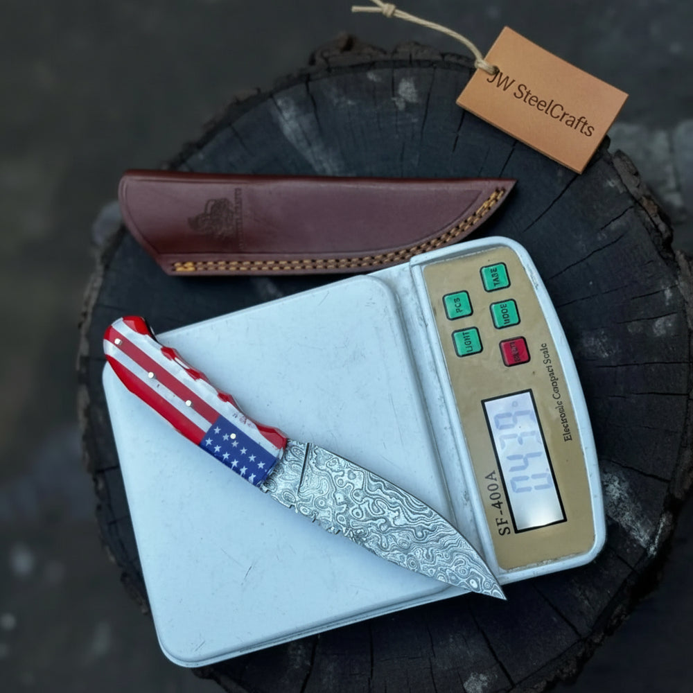 Damascus blade flag grip knife weight photo showing the knife on a compact digital scale over a dark tree stump.