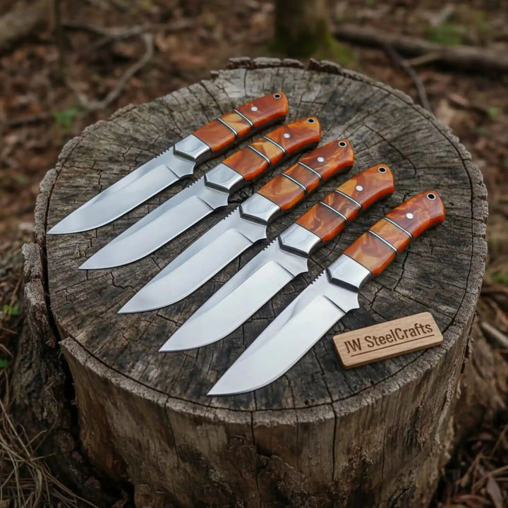 Distinctive serrated spine guards and orange swirl resin handles characterize this five-piece hunting knife collection on a stump