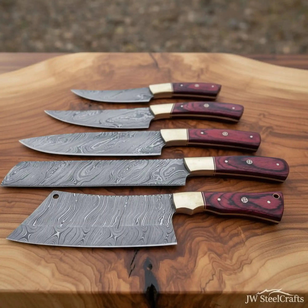 Damascus chef knife set with patterned steel blades and red wood handles displayed on wooden board.