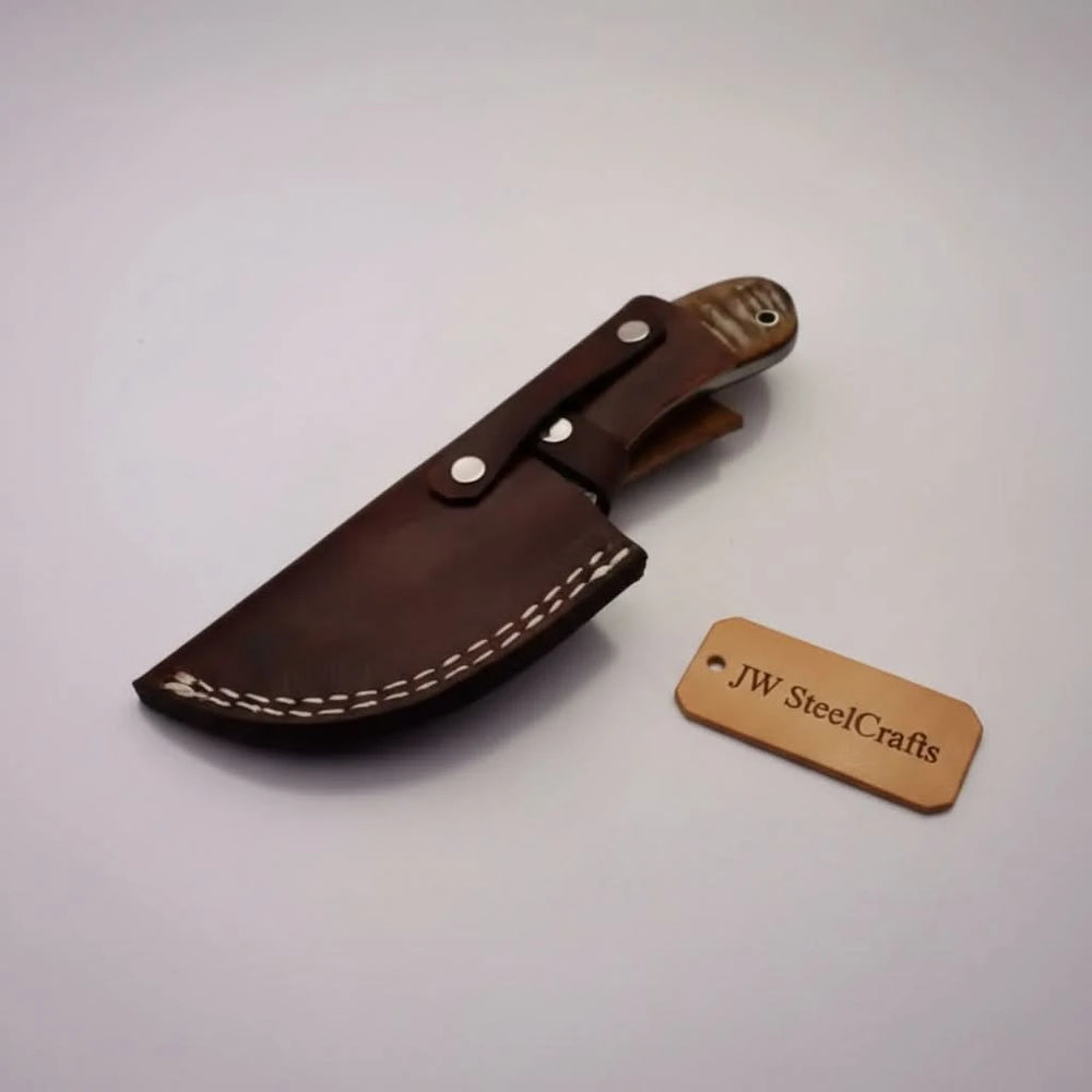 Stag handle gut hook Damascus knife by JW SteelCrafts with patterned blade, round finger hole, and tree stump display.