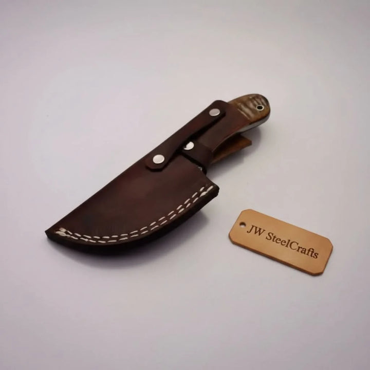 Stag handle gut hook Damascus knife by JW SteelCrafts with patterned blade, round finger hole, and tree stump display.