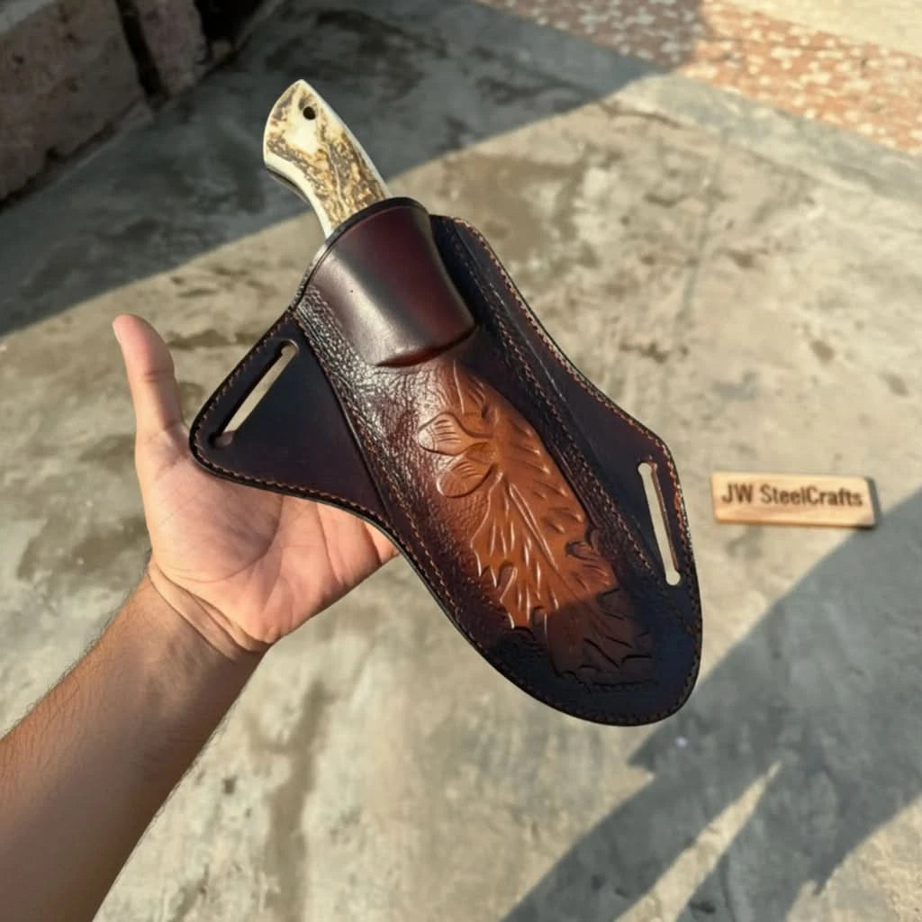 Embossed leather sheath holding a custom fixed blade knife with a stag-pattern handle in a person’s hand.