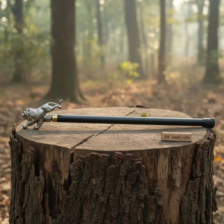 A handcrafted walking cane by JW SteelCrafts featuring a silver lion figurine handle, resting on a tree stump in a misty forest.