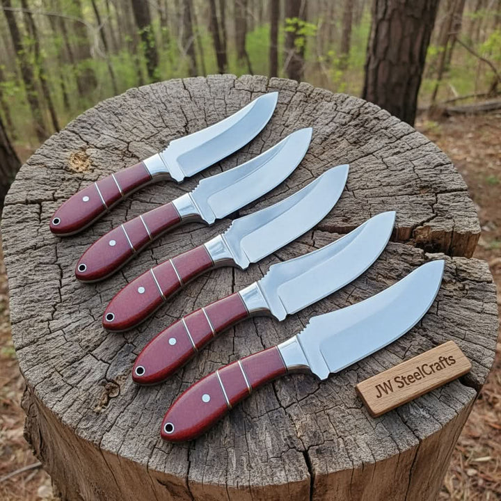 Laid in a graduated fan on a weathered forest stump, five skinner knives with burgundy micarta handles and silver liner accents