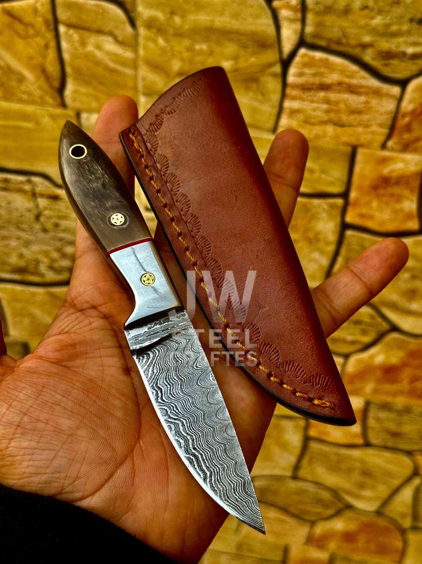 Knife with a leather sheath held by a hand against a stone wall background