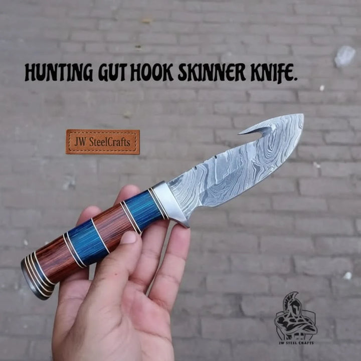 Custom fixed blade gut hook knife at campsite with Damascus blade, stacked blue brown grip, and weathered table.