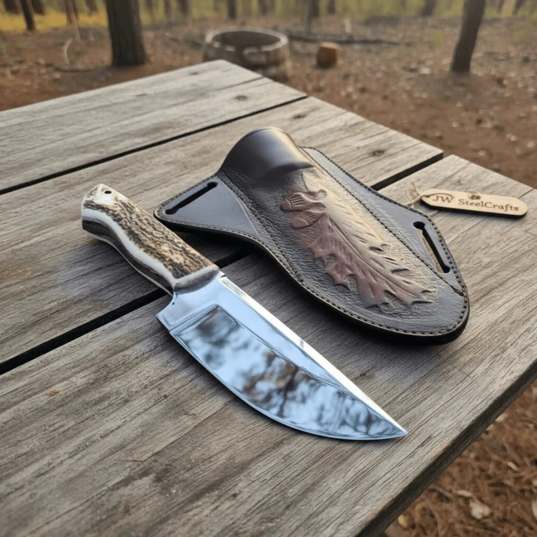 Polished steel bowie-style knife with a stag-pattern handle displayed next to a branded leather sheath.