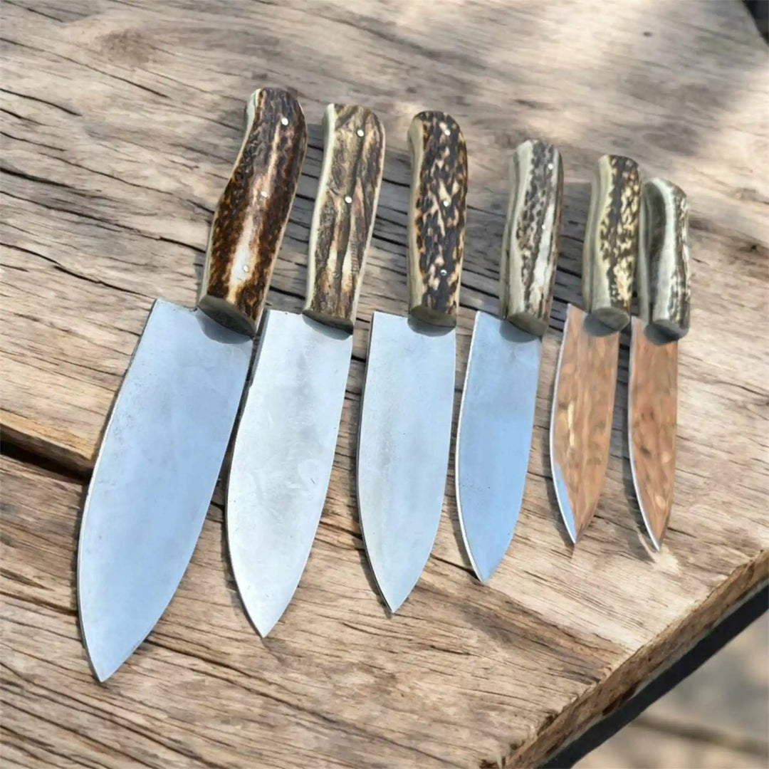 Rustic kitchen knife set with antler handles, six polished blades, and weathered wooden table surface.