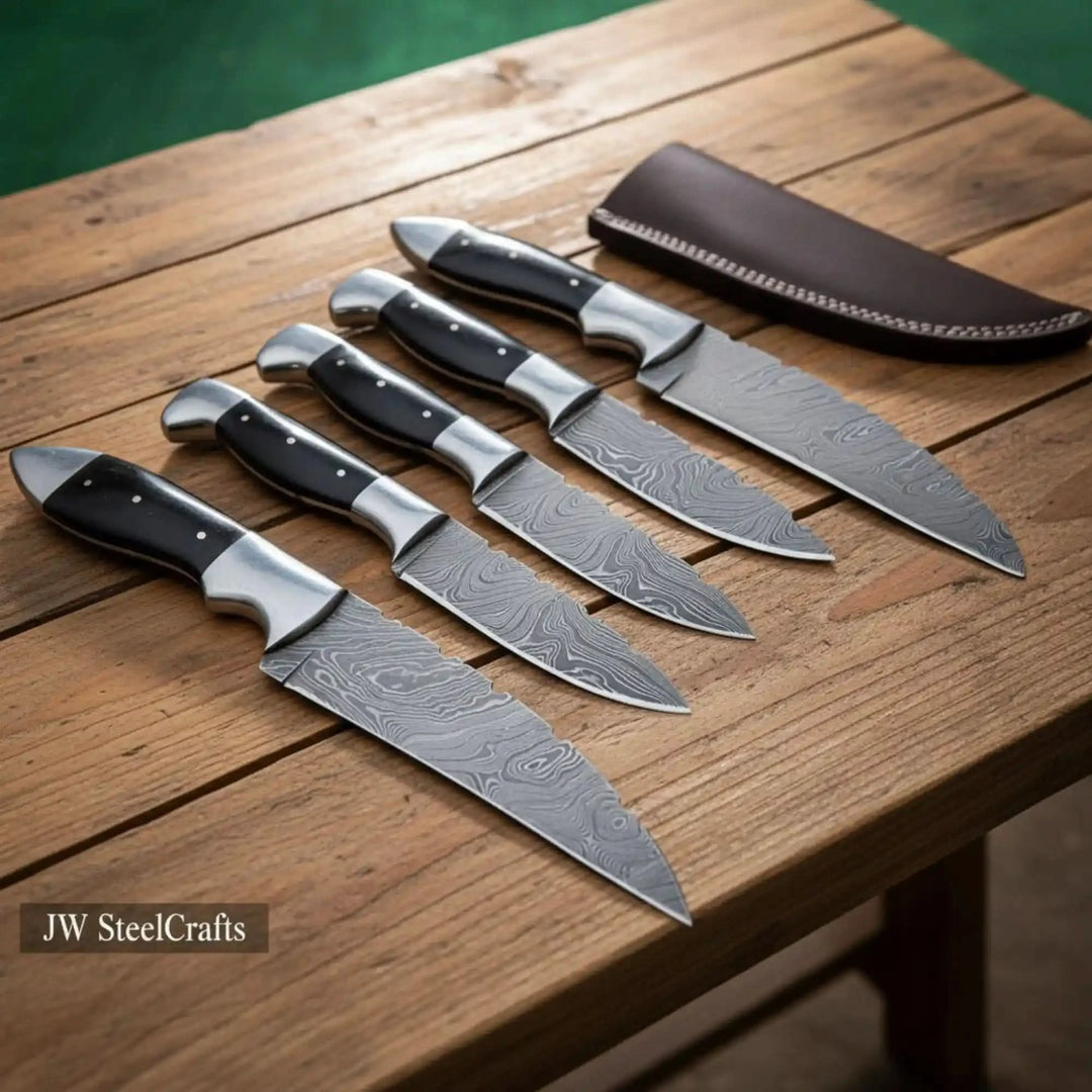 Premium Damascus steel hunting knife set featuring five full-tang Damascus bushcraft knives and Damascus field knives with black buffalo horn handles and polished steel bolsters displayed on rustic wooden table with dark brown leather sheath 