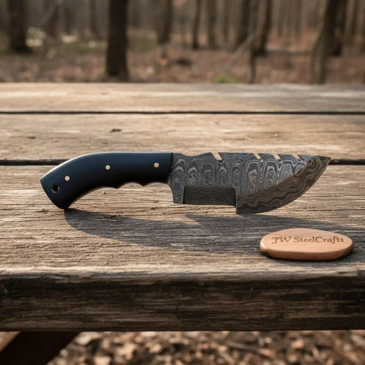 Etched steel cleaver knife product photo showing a sawback blade, black handle, and rustic outdoor stump display.