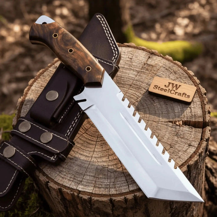 Large fixed blade survival knife displayed on a cut tree stump with leather sheath and JW SteelCrafts wooden label.