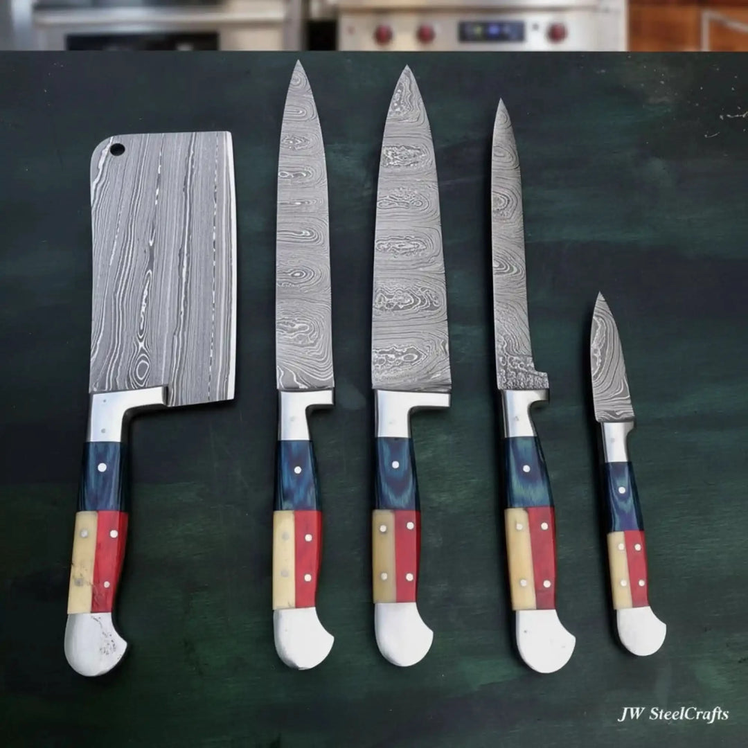 Complete Damascus steel kitchen knife set with five pieces including full-size cleaver all with matching Texas flag inspired tricolor resin handles on dark green kitchen surface
