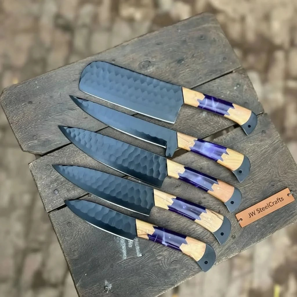 Top-down diagonal view of 5-piece hammered black blade culinary knife set featuring vivid purple resin and warm olive wood combination handles on a dark wooden surface
