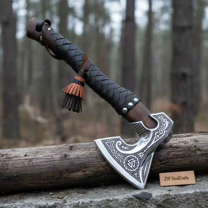 Rugged Viking axe with engraved blade artwork and textured black handle photographed on natural stone.