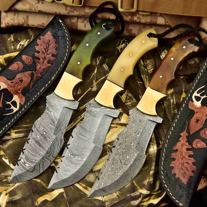 Tooled leather sheath three-knife set featuring etched Damascus blades, brass bolsters, and mixed handle colors.