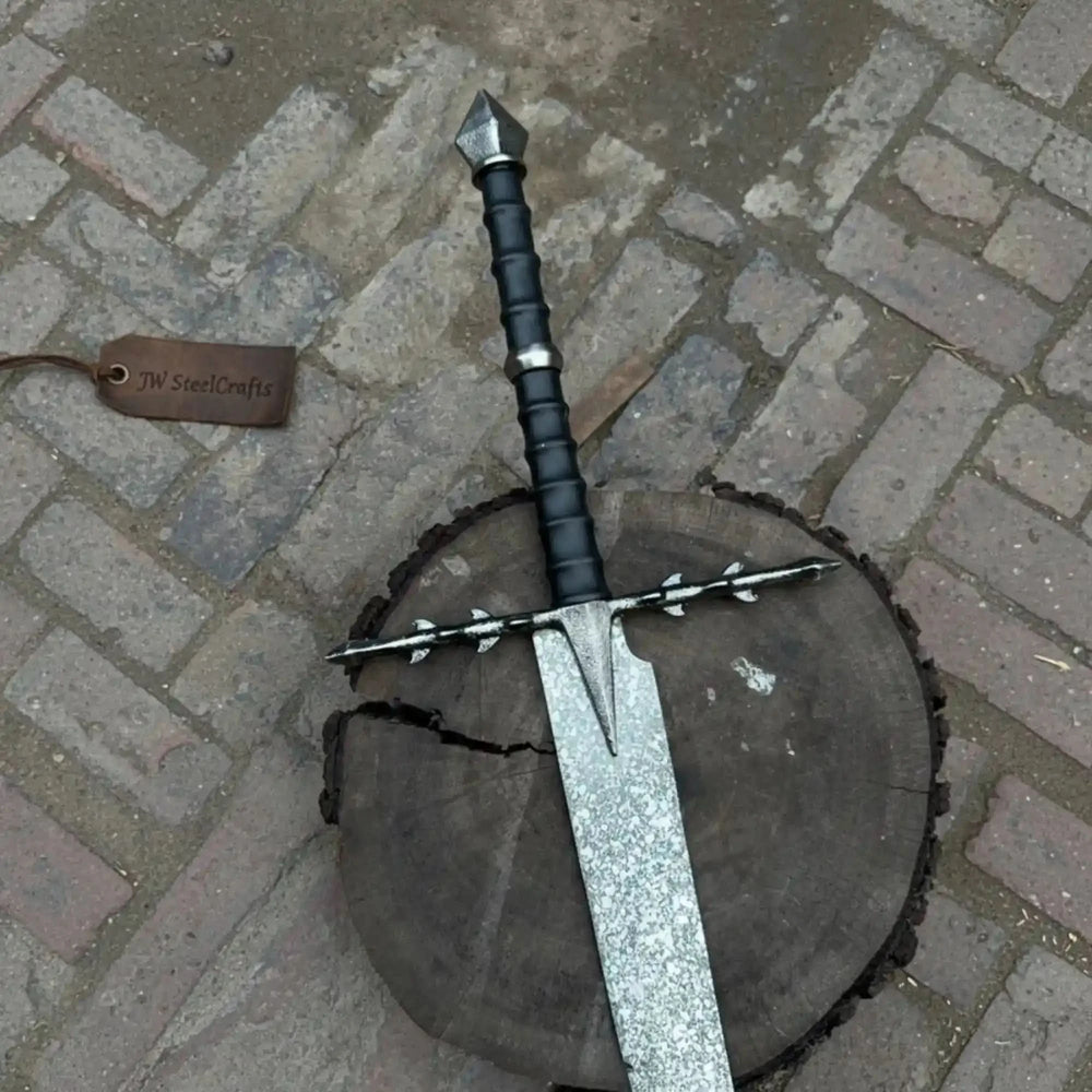 Close-up display of an ornate Damascus steel longsword showing the intricate silver crossguard, black wrapped two-handed grip, and long folded-pattern blade.