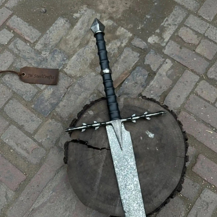 Close-up display of an ornate Damascus steel longsword showing the intricate silver crossguard, black wrapped two-handed grip, and long folded-pattern blade.