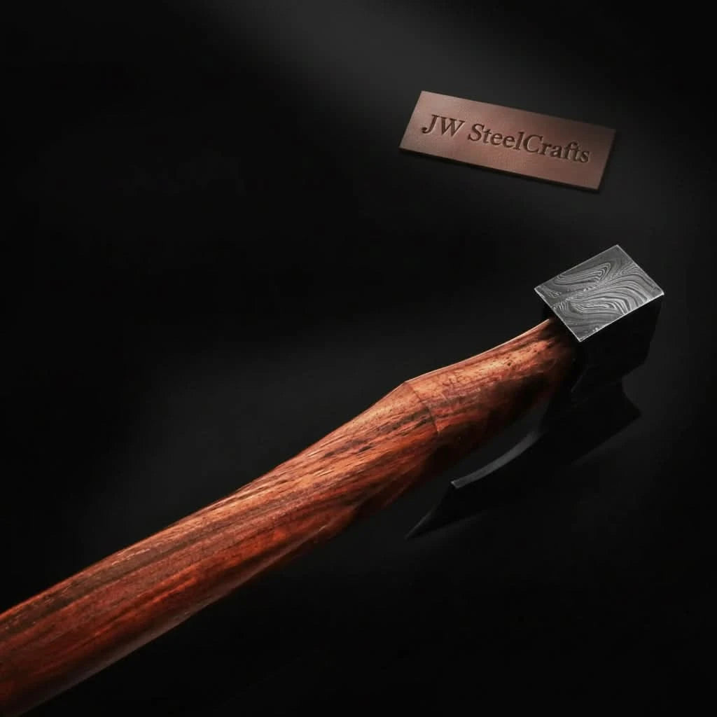 Close-up of a wilderness axe featuring Damascus steel craftsmanship and leather sheath on natural forest rocks.