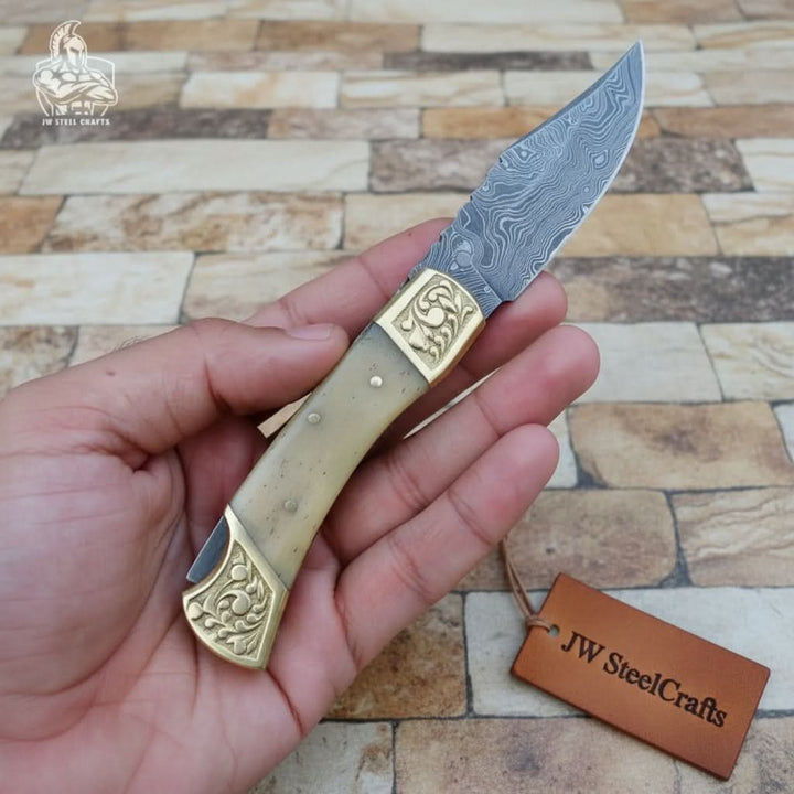     Frostvale Damascus EDC knife with brass detail fittings and slim patterned steel blade outdoors