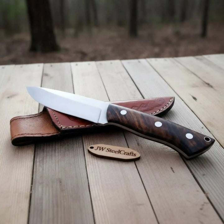 Handmade fixed blade knife featuring a dark wood handle, white pins, polished blade, and stitched brown leather sheath