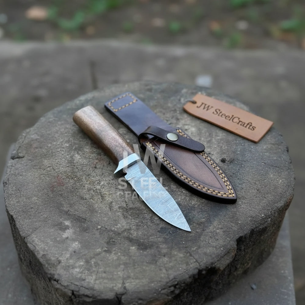 Compact outdoor hunting knife with a patterned steel blade and wood handle placed beside a snap-button leather cover.