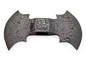     Double-headed Damascus steel battle axe with intricate layered patterns displayed on a rustic wooden platform in a misty forest setting.